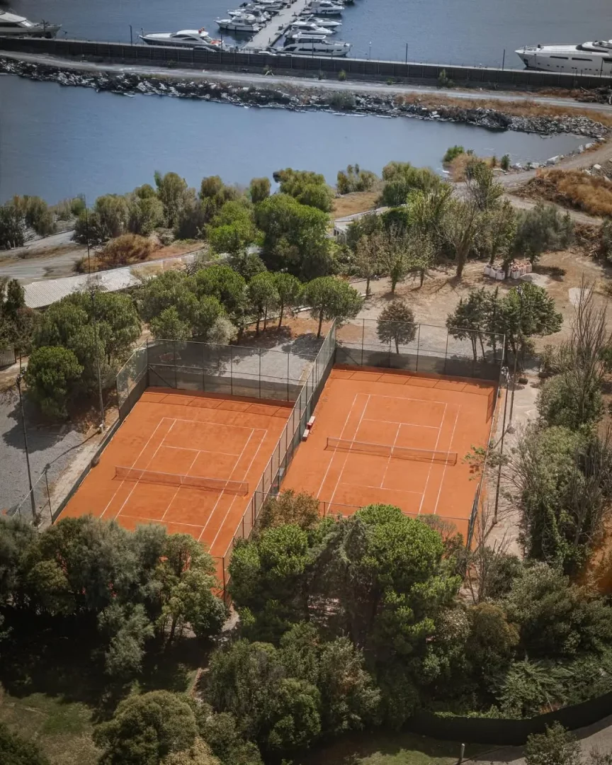 Hava fotoğrafında, yemyeşil ağaçlarla çevrili iki adet kırmızı kil tenis kortu görülmekte, arka planda ise birçok teknenin demirli olduğu mavi bir marina uzanmakta, bu tesisler Sheraton Istanbul Ataköy Tenis Kulübü'nün olanaklarını gösteriyor.