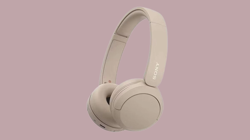 Pembe tonlarda pastel bir arka plan üzerinde sağa dönük hafif açıyla konumlandırılmış, açık bej rengi modern bir Sony WH-CH520 kablosuz kulaklık görseli. Ürünün sağ kulaklığının kafa bandında belirgin Sony logosu yer alırken, kullanıcı odaklı ergonomik ve sade tasarımı öne çıkıyor.