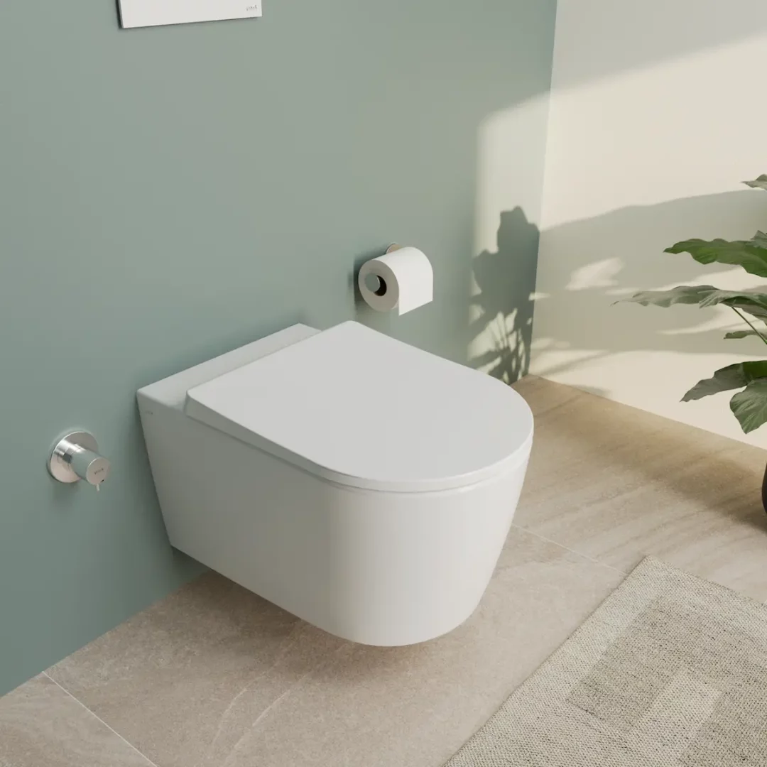 Açık yeşil ve beyaz tonlardaki modern bir banyo ortamında, duvara monte edilmiş, zarif ve minimalist beyaz Vitra QuantumFlush asma klozet, yanındaki krom taharet musluğu ve rulo tuvalet kağıdıyla birlikte şık bir görünüm sunarken, sağdaki dekoratif bitkiyle ortamın ferahlığını vurguluyor.