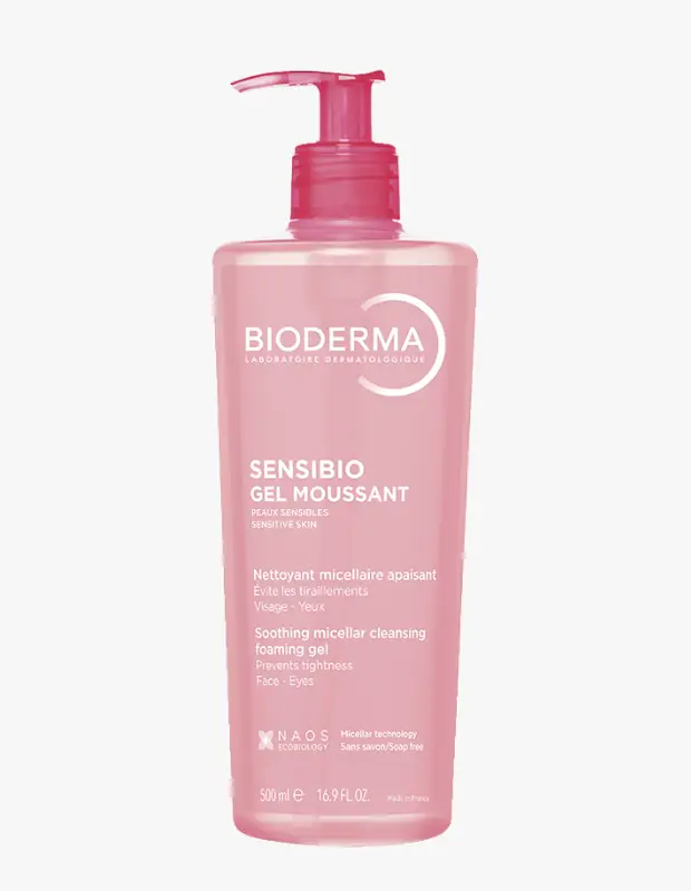 Pembe renkli, şeffaf bir şişede, üzerinde Bioderma markasının Sensibio Köpük Jel adı ve hassas ciltler için yatıştırıcı misel temizleme jeli özellikleri ile 500 ml hacminin belirtildiği, pembe pompalı kapağı olan bir ürün beyaz bir arka plan üzerinde dikey olarak sergileniyor.
