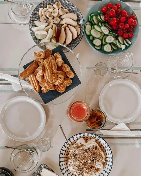 Kalymnos adasındaki Harrys Paradise Garden Taverna'da sunulan, dilimlenmiş muz, elma, salatalık, çeri domates, çeşitli hamur işleri ve granolalı yoğurt gibi zengin seçeneklerle dolu, iştah açıcı bir kahvaltı masası.
