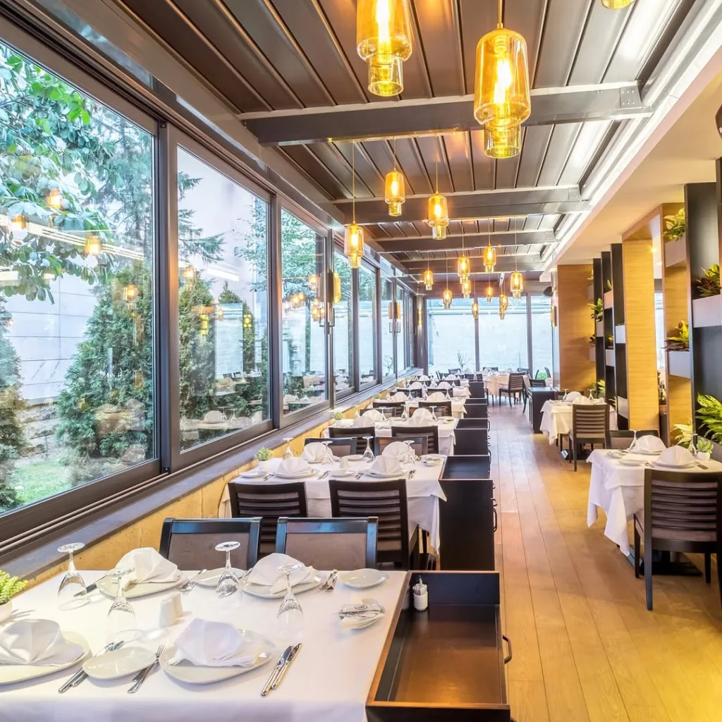 Sur Balık restoranının geniş ve aydınlık salonunda, tavandan sarkan amber renkli cam sarkıt lambaların aydınlattığı beyaz örtülü masalar misafirler için özenle hazırlanmış dururken, büyük pencerelerden yemyeşil bahçe manzarası içeriye huzurlu bir atmosfer katıyor.