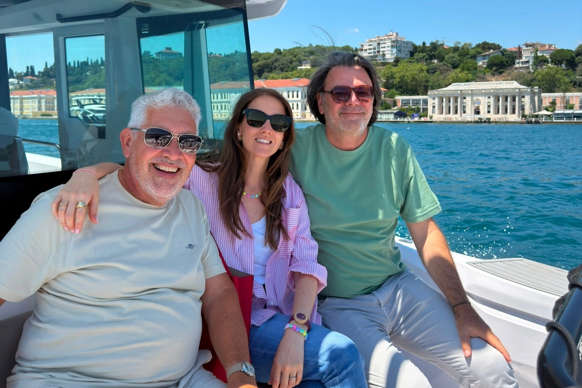 Bosphorus'un masmavi sularında, tarihi yapılar ve yeşil tepeler eşliğinde, güneşli bir günde teknede poz veren ve gülümseyen, sektörün önde gelen isimleri ve saat ustaları Alexia Genta, Enrico Barbasini ile Michel Navas.