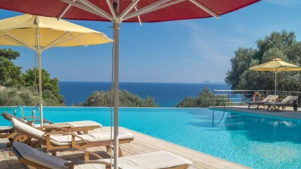 Armonia Bay Hotel'in turkuaz renkteki sonsuzluk havuzunun kenarından, masmavi denize nazır, konukların güneşlenip dinlenebileceği şezlonglar ve renkli şemsiyelerle donatılmış huzurlu bir manzara.