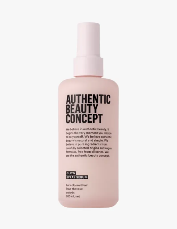 Açık pembe tonlarındaki Authentic Beauty Concept Glow Sprey Serum şişesi, boyalı saçlar için geliştirilmiş ışıltı veren bir bakım ürünü olduğunu belirten siyah ve beyaz yazılı etiketleriyle beyaz bir arka plan önünde dikey olarak konumlanmış.