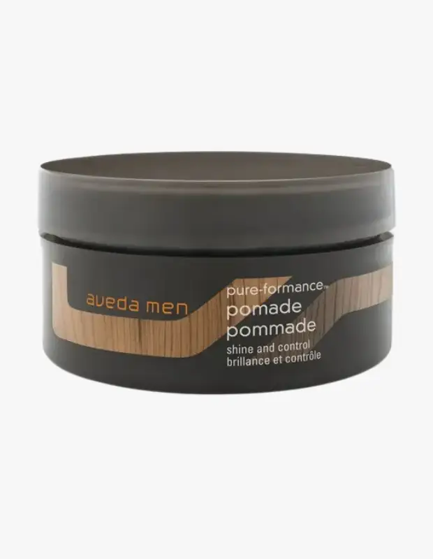 Koyu gri renkteki yuvarlak Aveda Men Pure-Formance Pomade kavanozu, üzerinde aveda men, pomade, shine and control ifadeleri ile ahşap dokulu şık bir tasarıma sahip olup saçlara parlaklık ve kontrol sağlamak için ideal bir saç şekillendirici üründür.