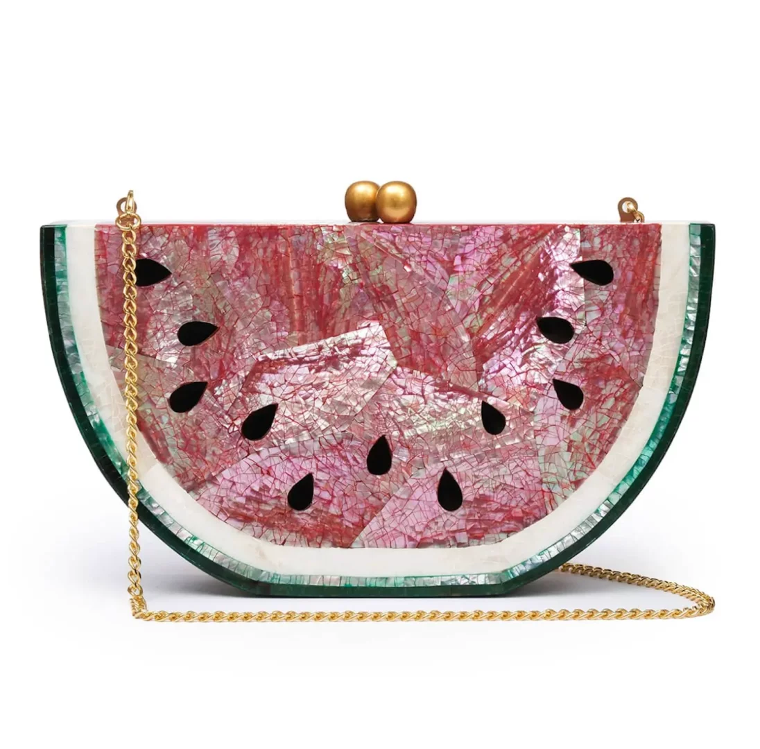 Karpuz dilimi şeklindeki bu göz alıcı clutch çanta, parlak pembe ve beyaz sedef kabuklarının mozaik desenleriyle bezenmiş, siyah çekirdek detayları, zarif altın rengi zincir sapı ve toka ile tamamlanmış eşsiz bir el işidir.