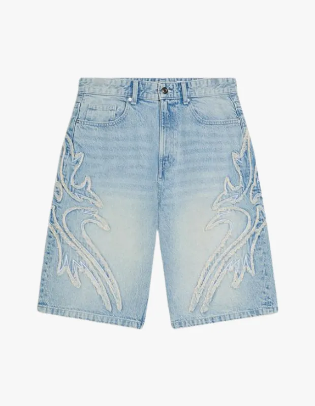 Diz hizasında biten, açık mavi eskitme görünümlü desenli denim bermuda şortun her iki bacağının yan tarafında, karmaşık ve yıpranmış kenarlı, kabartmalı parlak beyaz alev motifleri dikkat çekiyor.