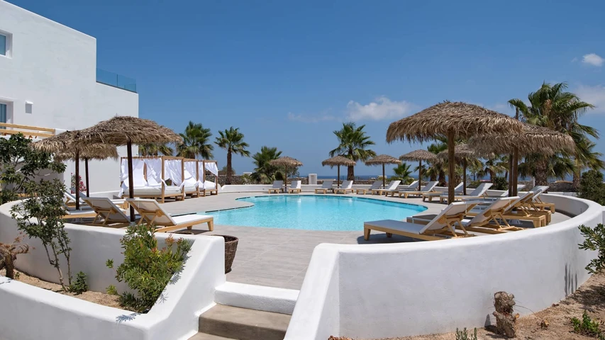 Casa Vitae Suites Kamari'nin beyaz minimalist mimarisiyle öne çıkan havuz alanı, masmavi gökyüzünün ve uzaktaki deniz manzarasının altında berrak suyu, palmiye ağaçları, hasır şemsiyeler ve beyaz örtülü cabanaların eşlik ettiği konforlu şezlonglarla dinlendirici bir Akdeniz atmosferi sunuyor.