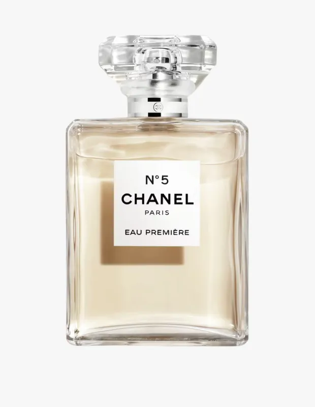 Beyaz bir arka plan üzerinde duran, içinde açık sarı renkli sıvısı bulunan, dikdörtgen cam şişesi ve şeffaf, geometrik şekilli kapağıyla ikonik Chanel N°5 Eau Première parfümü, üzerinde markanın adı ve ürün detayı yazan beyaz etiketiyle zarif bir şekilde sergileniyor.