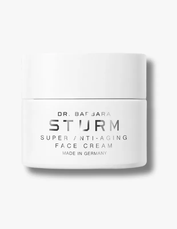 Parlak beyaz bir zemin üzerinde, zarif tasarıma sahip, beyaz renkli, köşeleri hafifçe yuvarlatılmış kare bir kavanozda duran Dr. Barbara Sturm Super Anti-Aging Face Cream; kavanozun ön yüzünde Dr. Barbara Sturm markası, büyük ve yansıtıcı gümüş renkli harflerle STURM yazısı ile altında Super Anti-Aging Face Cream ve Made in Germany ibareleri açıkça görülmektedir.