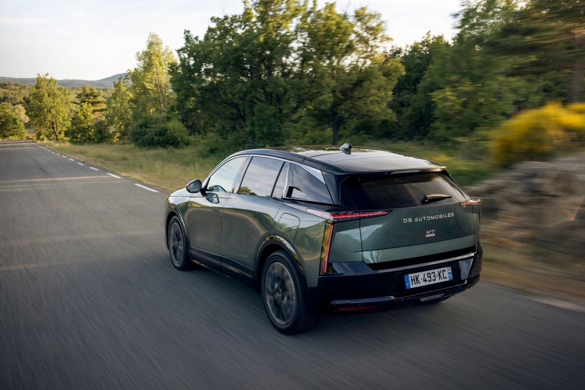 Koyu yeşil renkli, lüks DS N7 elektrikli premium SUV, ağaçlarla çevrili virajlı bir yolda dinamik bir şekilde ilerlerken, 740 km menzil vaat eden modelin modern arka tasarımı ve keskin hatlara sahip stop lambaları belirgin biçimde öne çıkıyor.