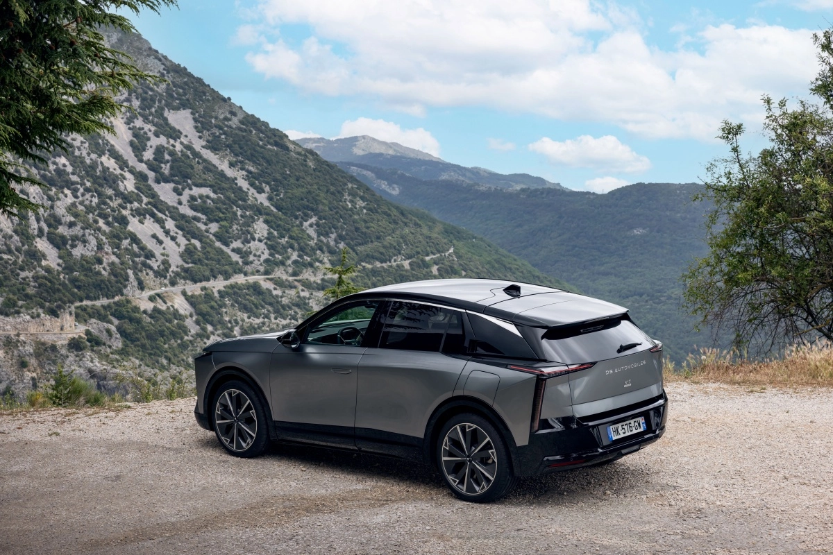 Gri renkli, şık DS N7 lüks elektrikli premium SUV, dağlık ve ağaçlık bir manzara önünde toprak bir yolda hafif açıyla park edilmiş olarak, aracın dış tasarımının ve arka kısmının modern hatlarını sergiliyor.
