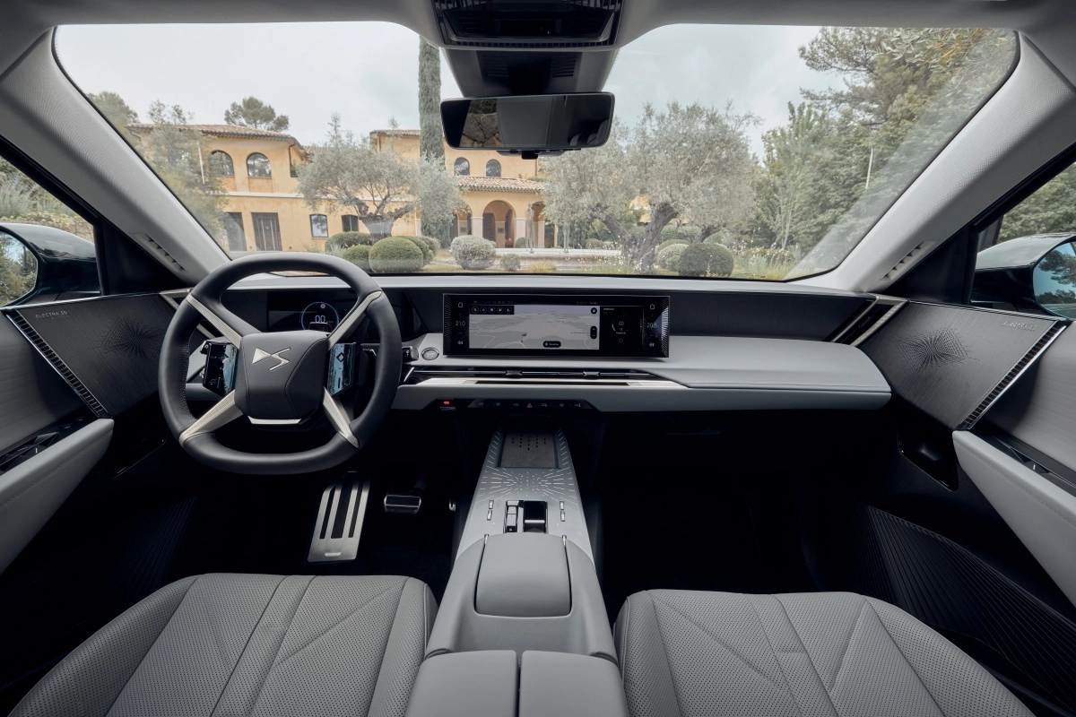 DS N7 lüks elektrikli premium SUV'nin modern ve şık iç mekan ön konsol tasarımı, büyük bir bilgi-eğlence ekranı, gri deri koltuklar ve dışarıda görünen villanın lüks ortamıyla birleşerek konforlu bir sürüş deneyimi vadediyor.