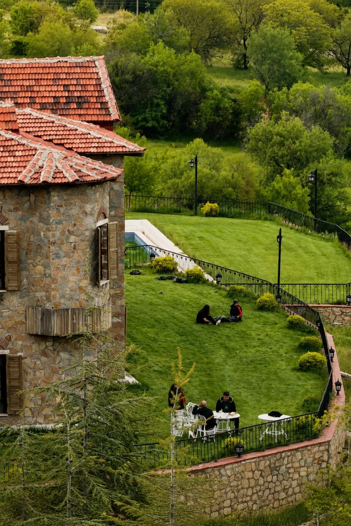 Eskibağlar Boutique Hotel'in taş duvarlı binasının kırmızı kiremitli çatısı önünde uzanan yemyeşil bahçesinde, bazı misafirler eğimli çimlerde dinlenirken, diğerleri ferforje korkuluklu terasta masalarda oturup sohbet ederek keyifli vakit geçiriyor, etrafı saran ağaçlar huzurlu bir butik otel atmosferi sunuyor.