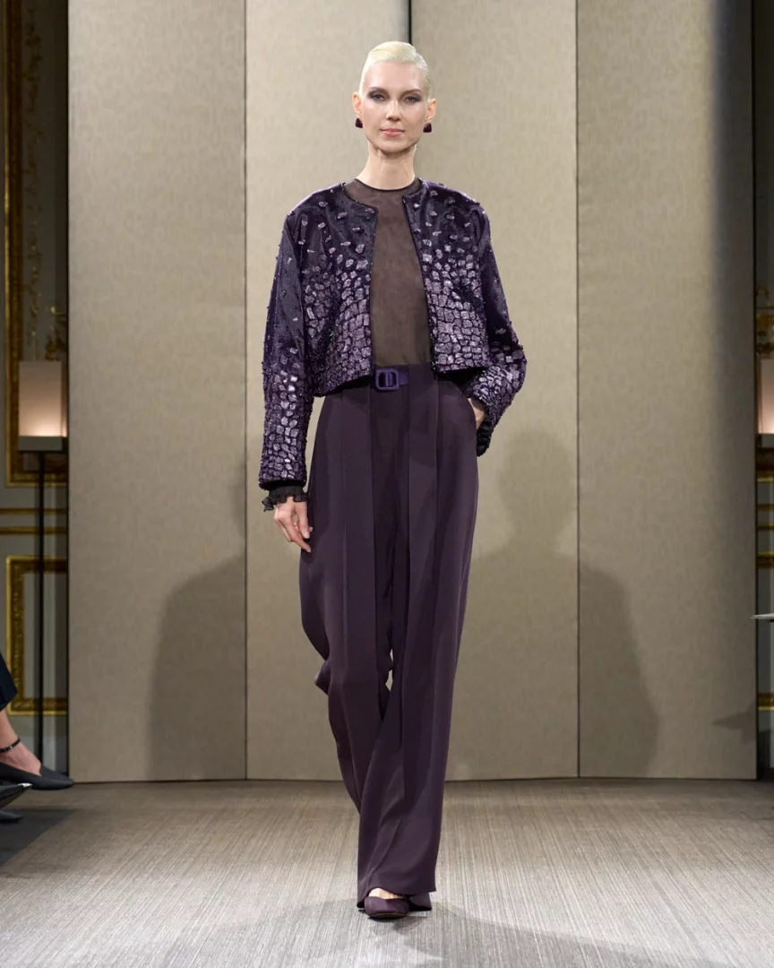 Giorgio Armani Privé Sonbahar-Kış 2026 couture defilesinden, podyumda yürüyen model, parlak işlemeli mor kısa ceketi, şeffaf bluzu ve beli kemerli geniş paça pantolonuyla Paris Haute Couture Moda Haftası'nın dikkat çeken anlarından birini sunuyor.