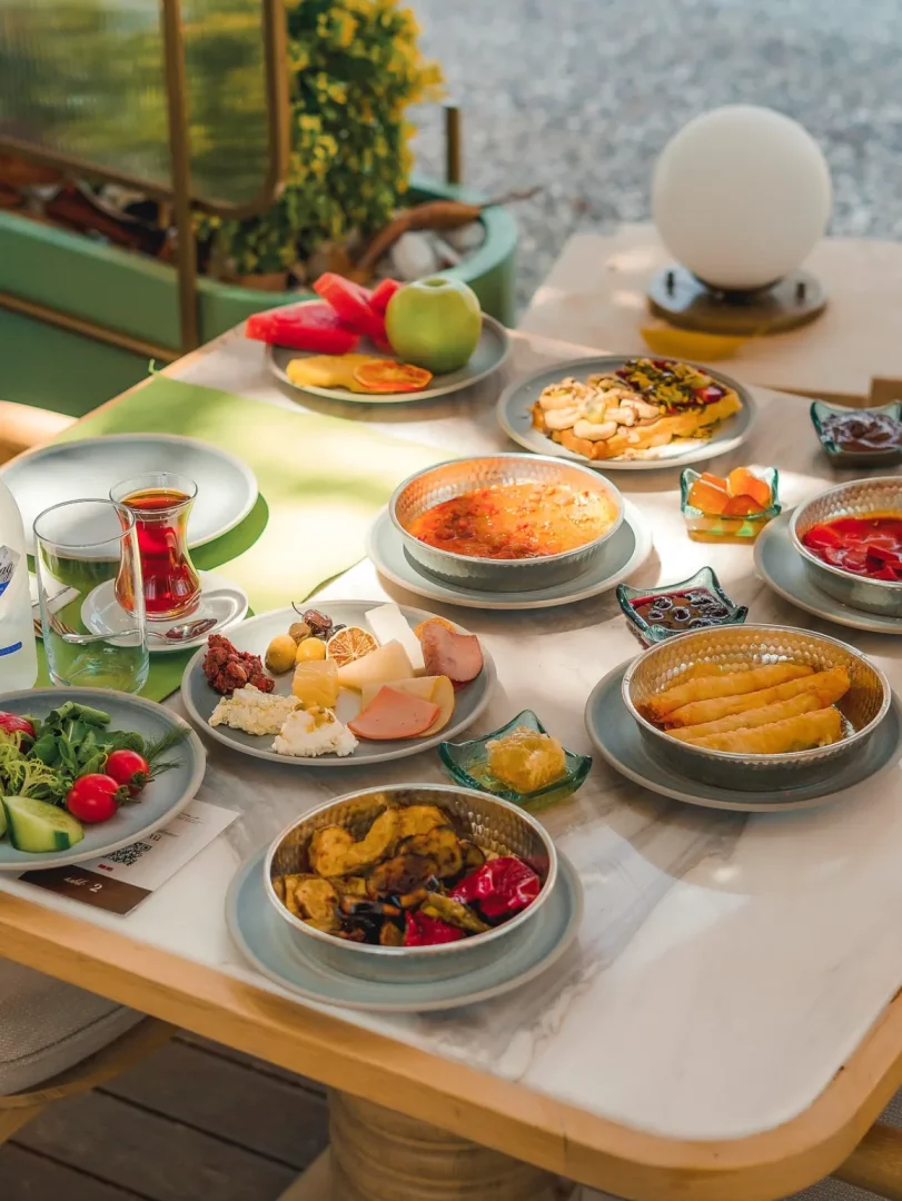Göcek'te gezilecek yerlerden biri olan bu mekanda, taze meyveler, peynir çeşitleri, zeytinler, salamlar, menemen, sigara böreği ve ızgara sebzeler gibi bol çeşitli geleneksel lezzetlerle dolu, mermer bir masanın üzerinde özenle sunulan zengin bir Türk kahvaltısı sofrası.