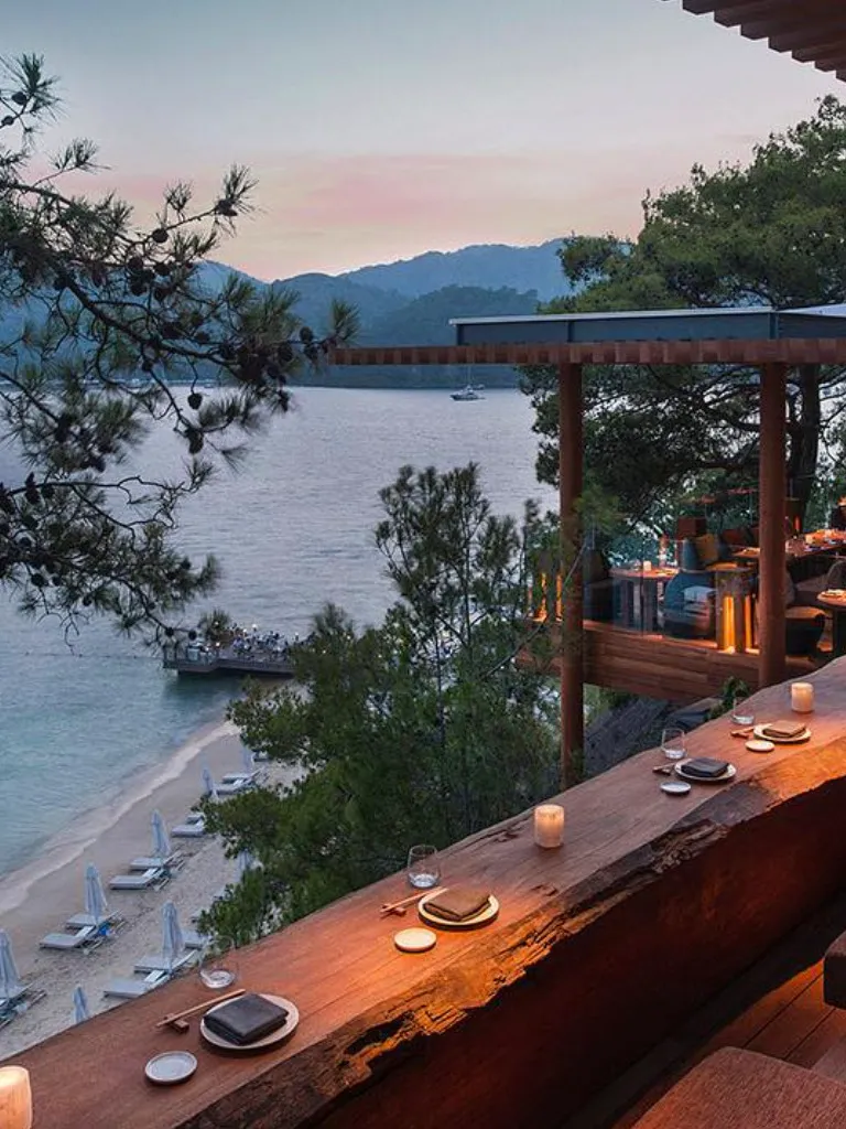 Göcek'te gezilecek yerler arasında öne çıkan bu eşsiz restoranın ahşap barında, gün batımının büyüleyici ışıkları altında, denize nazır uzanan kumsaldaki şezlongları ve iskeleyi, karşıdaki dağ siluetleriyle birlikte seyretmek tarifsiz bir huzur sunuyor.