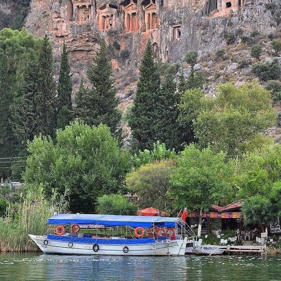 Mavi tenteli beyaz bir tekne, can simitleriyle donatılmış halde, yemyeşil ağaçların ve ardındaki görkemli Lykia kaya mezarlarının yükseldiği nehirde sakin bir şekilde duruyor, Göcek gezilecek yerler listesindeki eşsiz doğal ve tarihi güzelliklerden birini gözler önüne seriyor.