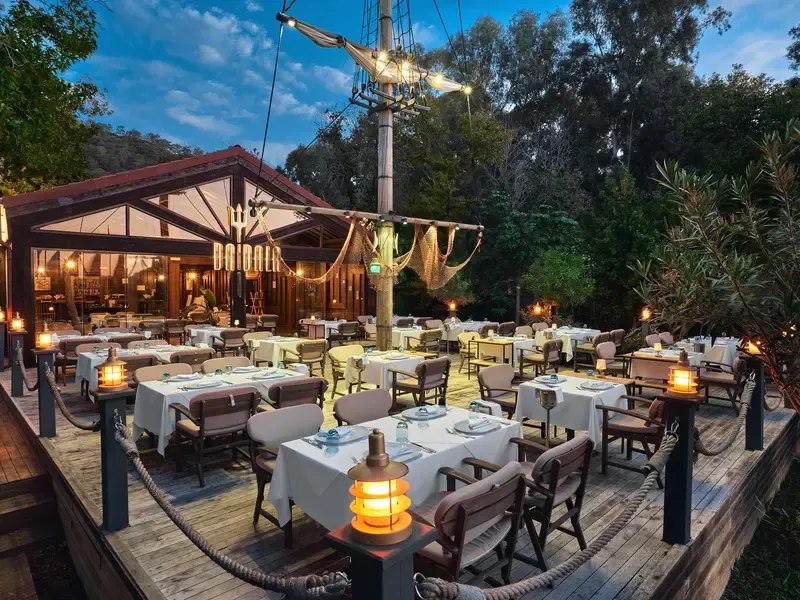 Göcek'in gezilecek yerlerinden biri olan Daidala restoranının, akşam ışıklarıyla aydınlanan ahşap terasında, deniz temalı dekorasyon ve yemyeşil ağaçlarla çevrili şık masalar konukları ağırlamaya hazır.