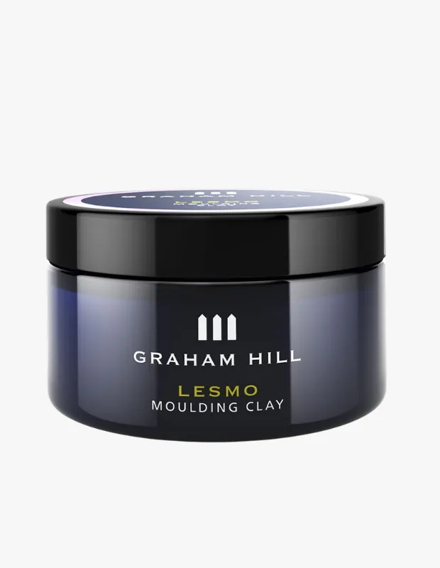 Graham Hill Lesmo şekillendirici kil, üzerinde markanın üç dikey çubuklu logosu ve beyaz metinle Graham Hill, Lesmo, Moulding Clay yazıları bulunan, koyu lacivert tonlarında parlayan, siyah kapaklı, şık bir saç şekillendirme ürünü kavanozudur.