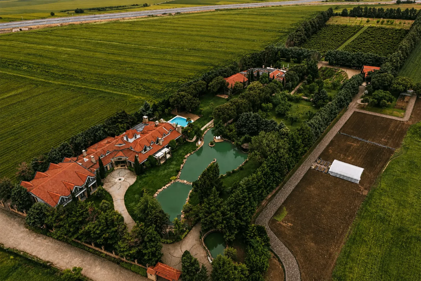Havadan çekilen bu geniş malikane görüntüsünde, yemyeşil tarlaların ortasında, kırmızı çatılı binalar, içinde göletler, bir yüzme havuzu ve yoğun ağaçlık alanlarla çevrili, arkasında otoyol uzanan bir büyükanne harikalar diyarı gibi bir cennet köşesi.