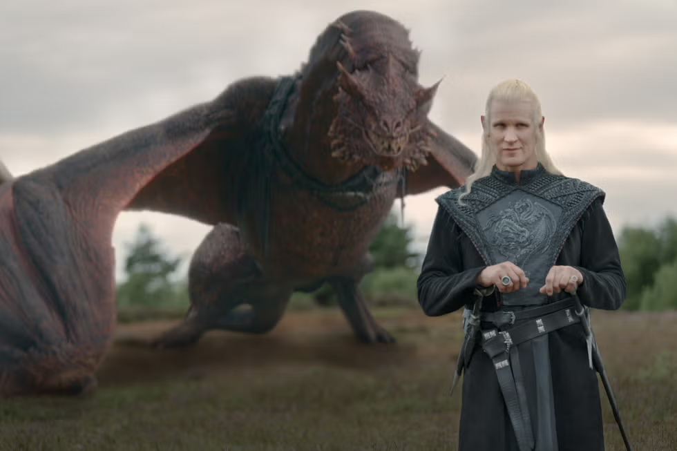 Sarı saçları, omuzlarında ejderha armalı siyah cübbesiyle Prens Daemon Targaryen, bakışlarını izleyiciye yöneltirken, arkasında kızıl-kahverengi pullara sahip, uzun ve ince gövdeli ejderhası Caraxes, kanatları hafifçe açık vaziyette yeşillik bir arazide durarak Ejderhaların Dansı'nın en kritik karakterlerinden ikisini gözler önüne seriyor.