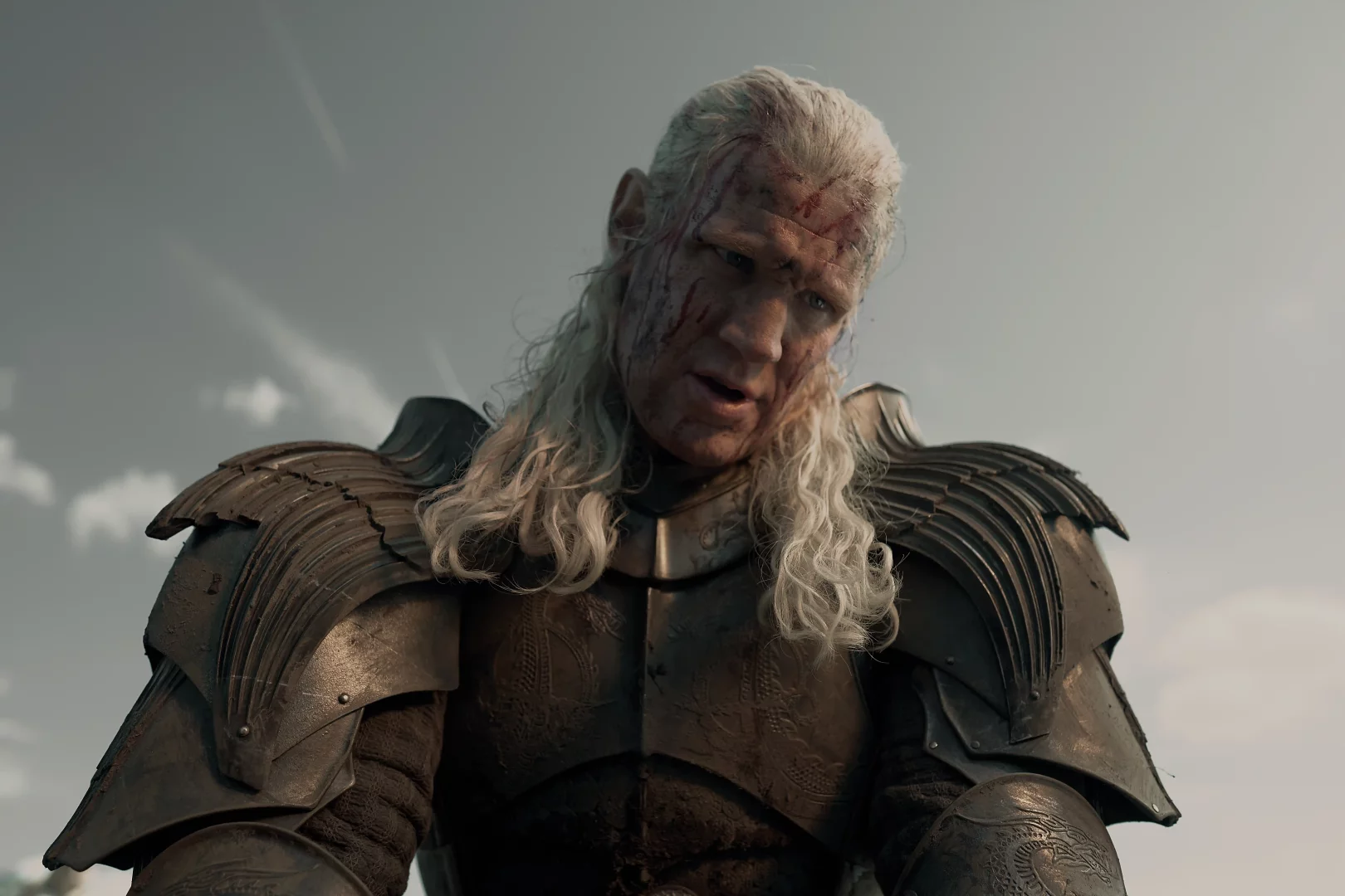 House of the Dragon dizisinden, yüzü kanlar ve yaralar içinde, yorgun ama kararlı bir ifadeyle koyu renk zırhını giymiş Prens Daemon Targaryen, Ejderhaların Dansı'ndaki çetin mücadeleyi ve 3. sezonun acımasızlığını gözler önüne seriyor.