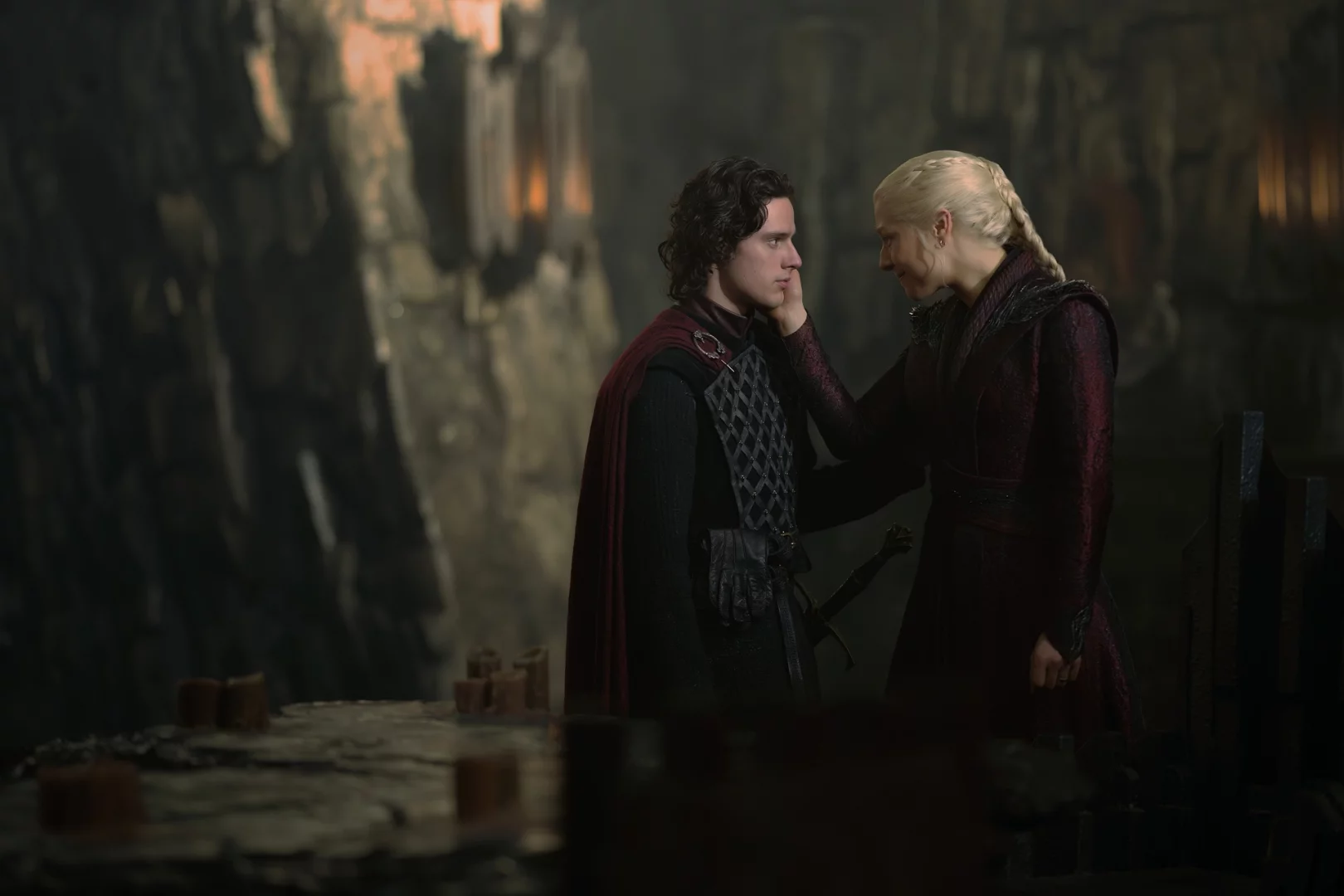 House of the Dragon dizisinden Rhaenyra Targaryen, loş ışıklı taş bir odada oğlu Jacaerys Velaryon'un yüzünü şefkatle okşarken, aile bağlarının Demir Taht mücadelesindeki karmaşıklığını ve kırılganlığını gözler önüne seriyor.