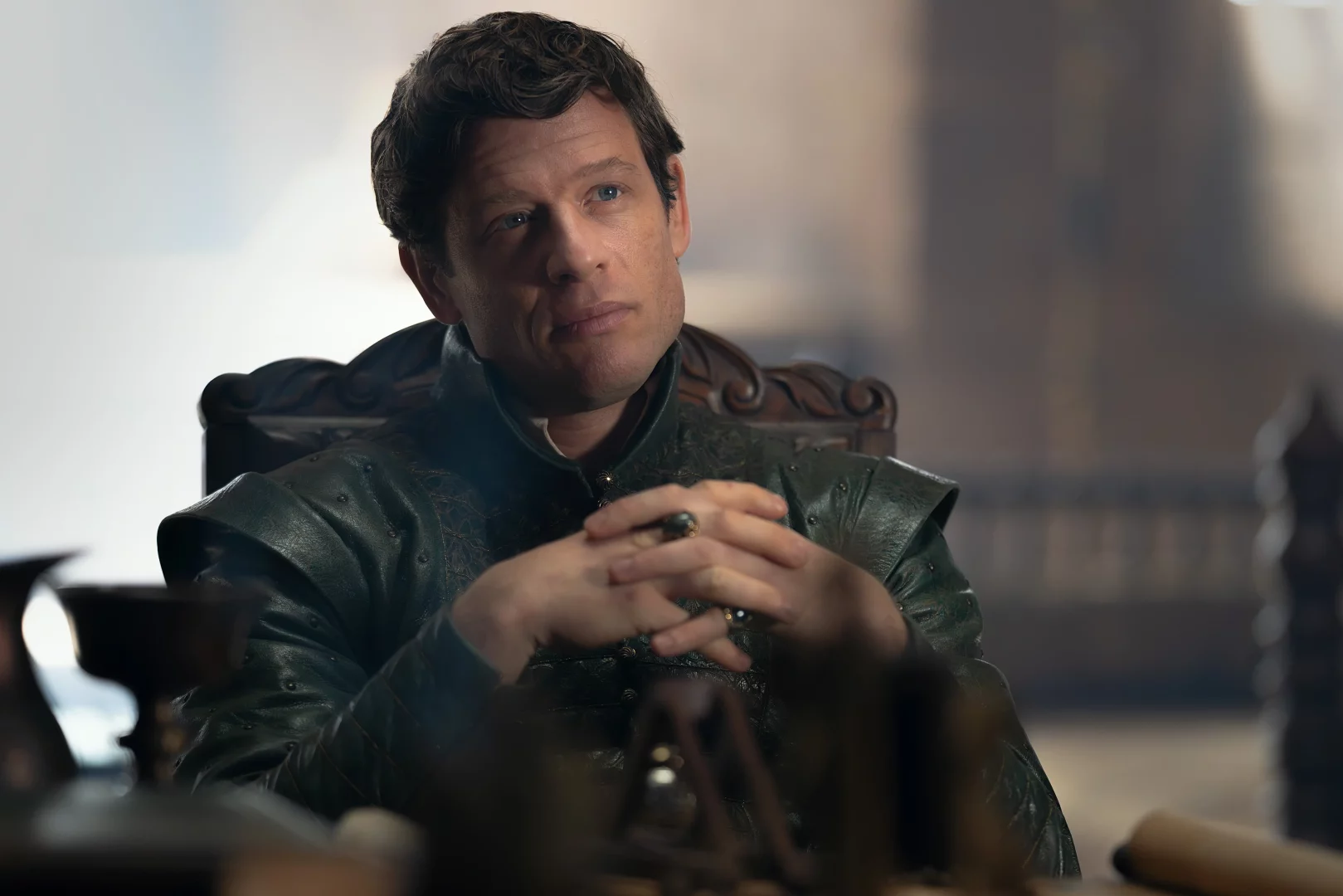 House of the Dragon dizisinden, koyu yeşil işlemeli kıyafetler giyen, ellerini önünde kavuşturmuş ve yüzünde düşünceli bir ifade olan Ormund Hightower, Yeşiller'in kritik askeri liderlerinden biri olarak 3. sezon finaline yaklaşan Ejderhaların Dansı iç savaşında önemli bir figür.