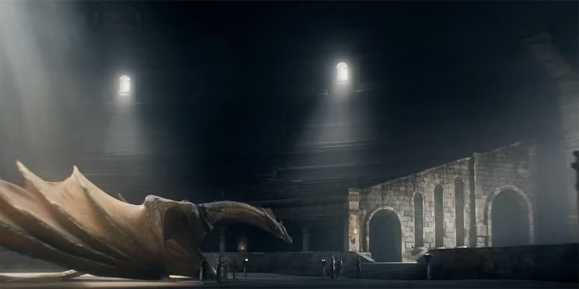 House of the Dragon dizisinden, yüksek pencerelerden gelen ışık huzmelerinin aydınlattığı geniş ve karanlık bir taş salonda, Ejderhaların Dansı'nda önemli bir rol oynayan altın pullu ejderha Sunfyre'ın yerde uzanmış, çevresinde küçük insan figürlerinin olduğu dramatik bir an.