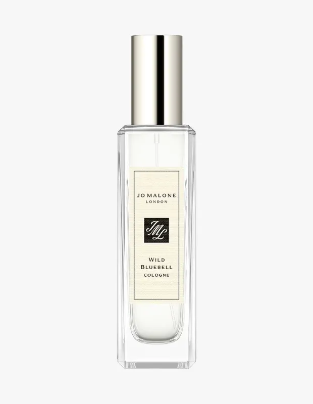 Beyaz bir zeminde dikey olarak konumlandırılmış, şeffaf camdan yapılmış Jo Malone London Wild Bluebell Kolonya şişesi, parlak gümüş rengi kapağı ve üzerinde marka logosu ile ürün adı yazılı bej etiketiyle dikkat çekiyor.