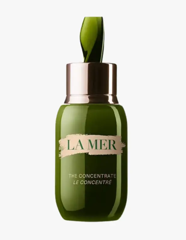 Beyaz bir arka plan üzerinde, La Mer The Concentrate yenileyici serumun koyu yeşil, estetik şişesi sergileniyor; şişenin üzerinde La Mer ve The Concentrate yazıları, bakır renkli metal halka ve yaprak formunda yeşil damlalık dikkat çekiyor.