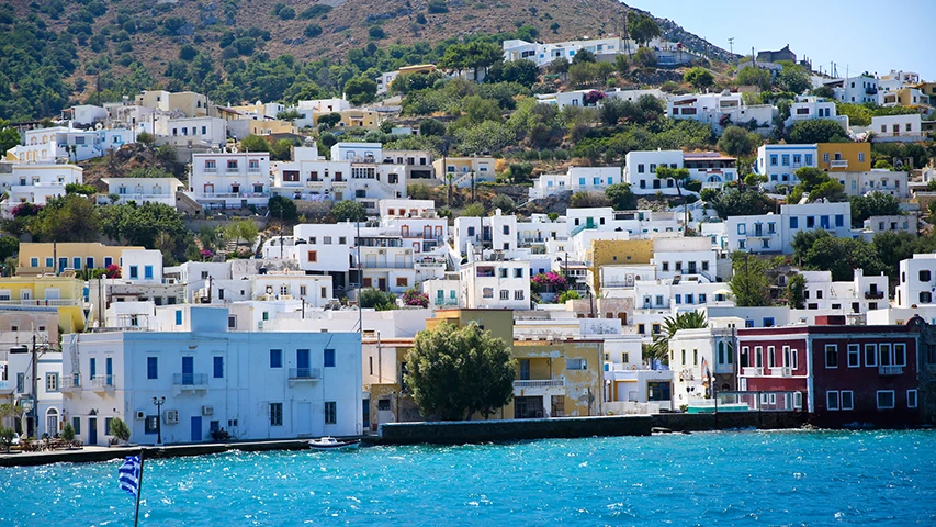 Leros kıyısında, masmavi denizin üzerinde yamaçlara kurulmuş, beyaz badanalı ve renkli pencereli binaların oluşturduğu büyüleyici bir köy manzarası, Leros'ta konaklama seçeneklerini düşünen misafirler için otellerin cazibesini yansıtıyor.