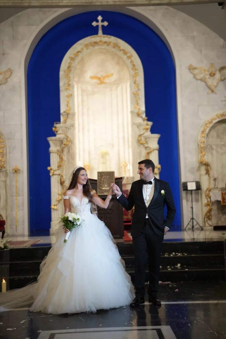 Lidya Amun ve Cem Amun, Mor Efrem Süryani Kadim Ortodoks Kilisesi’ndeki düğünlerinin en özel anlarından biri olan kilise töreninde, Lidya kabarık beyaz gelinliği ve tacıyla zarifçe gülümsüyor, Cem ise şık siyah smokiniyle ona bakarak mutlulukla karşılık veriyor, bu unutulmaz an İki Gelenek ve büyük Aşklarının kutsal birleşmesini mavi ve altın rengi detaylarla süslü görkemli kilise atmosferinde sergiliyor.