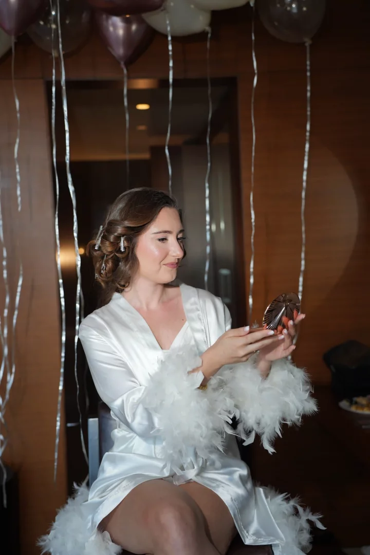 Lidya Amun, düğün gününe hazırlık anında beyaz tüylü sabahlığı, Hollywood dalgalı saçları ve ışığı yansıtan doğal makyajıyla, aynaya bakarak masalsı gelin görünümünü tamamlarken mutlu hikayesinin başlangıcına dair heyecanını yansıtıyor.