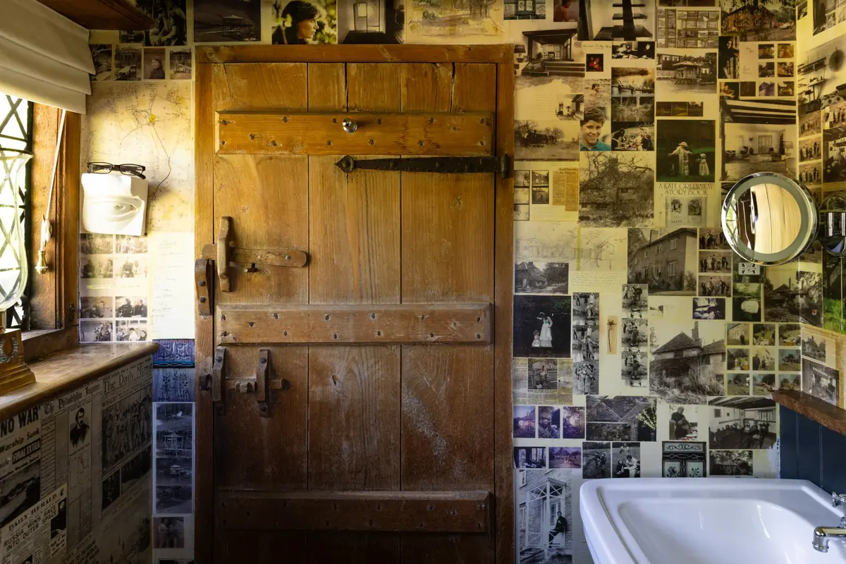 Rustik ahşap kapı ve pencereli bir köşeyle çevrili bu eski evin duvarları, yüzlerce siyah beyaz fotoğraf, çizim, harita ve gazete kupüründen oluşan yoğun bir hatıra duvarıyla kaplı olup, sağ alt kısımda beyaz bir lavabo ve yuvarlak bir ayna yer almaktadır.