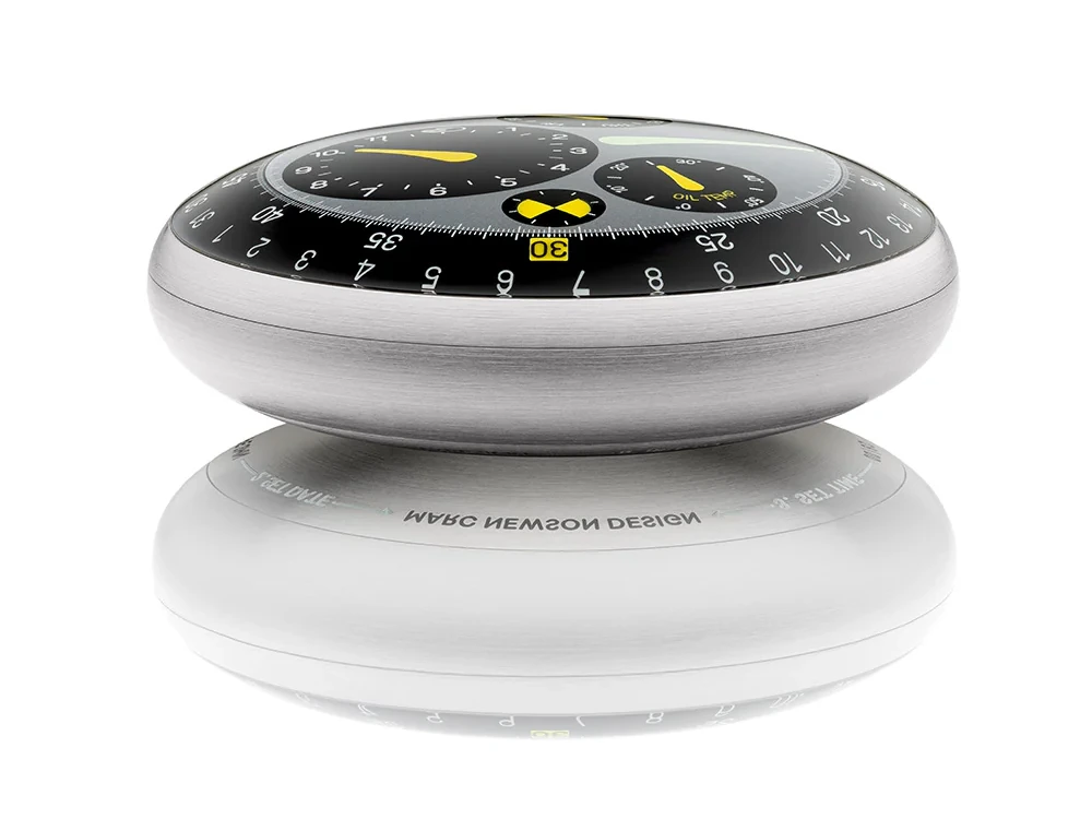 Beyaz yansımalı zeminde, parlak fırçalanmış metal kasaya sahip Marc Newson tasarımı Ressence Type 3 saati, sarı ibreler ve OIL TEMP göstergesi içeren siyah disk kadranıyla yenilikçi ve sofistike bir estetiğe sahip.