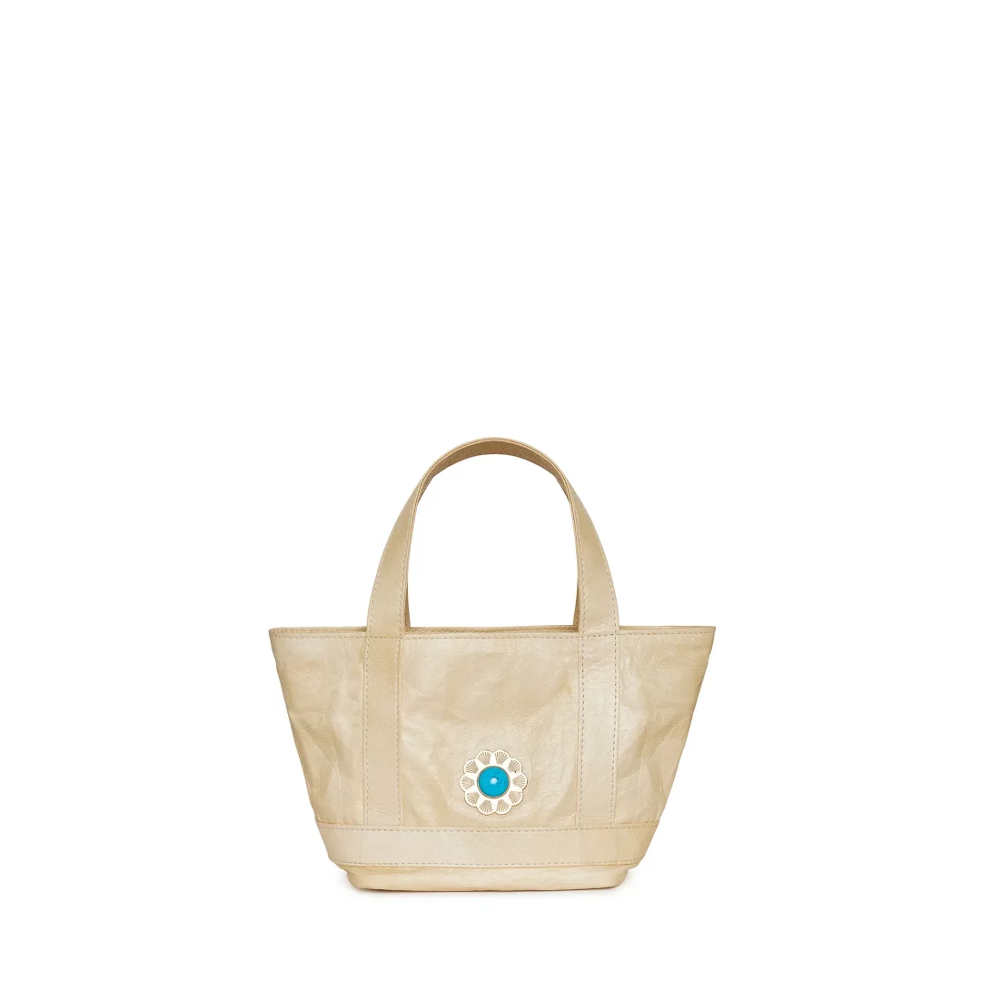 Parlak beyaz bir arka plan üzerinde sergilenen, Mehry Mu'nun imzasını taşıyan bej tonlarındaki Micro Cosima sunburst tote çanta, ön yüzündeki turkuaz taşlı ve metalik güneş deseniyle dikkat çekiyor.