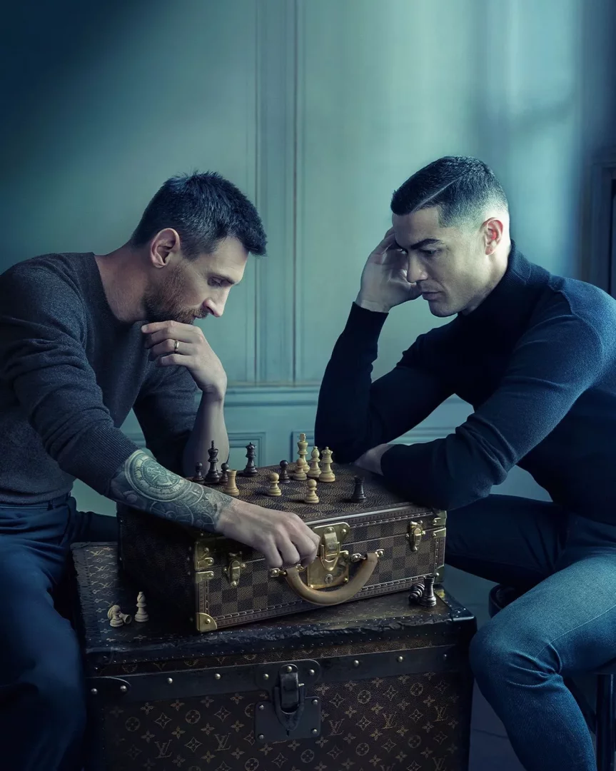 Gri kazaklı Lionel Messi kollarındaki dövmelerle bir Louis Vuitton sandığı üzerindeki satranç tahtasında bir taşa dokunurken, siyah balıkçı yaka kazağıyla Cristiano Ronaldo derin düşüncelere dalmış, iki futbol efsanesi satranç tahtası başında kariyerlerinin uzun ömürlülüğünü ve kıyasıya rekabetlerini yansıtan bu stratejik oyunu oynuyor.