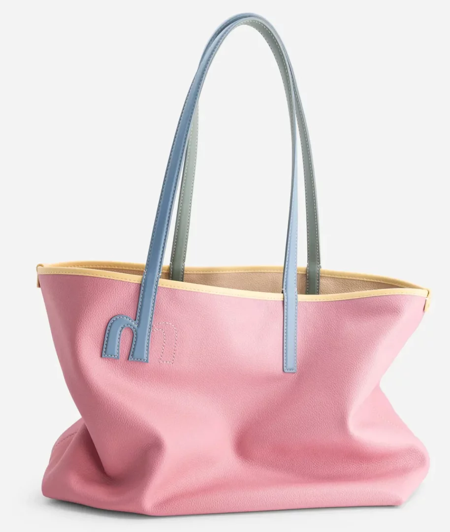 Pastel pembe renkte, uzun mavi ve gri sapları olan, ön yüzünde mavi M harfi şeklinde detay bulunan ve sarı kenar şeridiyle tamamlanmış, yumuşak görünümlü Mlouye marka büyük bir tote çanta beyaz fonda sergileniyor.