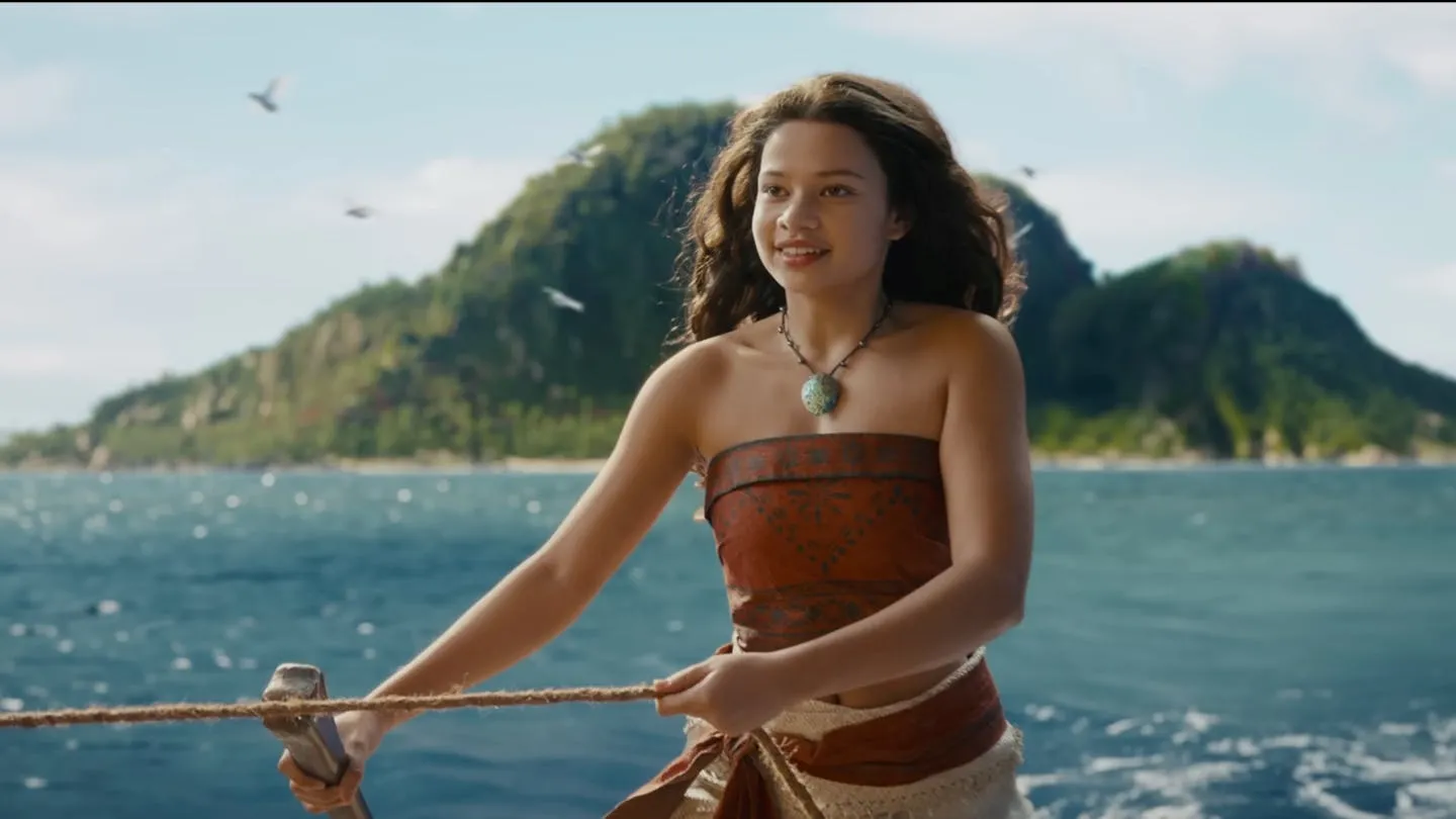 Moana filminden canlı aksiyon uyarlamasının bir karesinde, genç Moana, uzun dalgalı saçları, geleneksel deseni andıran askısız bluzu ve boynundaki turkuaz kolyesiyle bir ipi tutarken denizde gülümsüyor; yemyeşil adalar ve masmavi denizin oluşturduğu fon, Burak Göral'ın vizyonda izlemeye değer filmler arasında önerdiği bu macerayı vurguluyor.