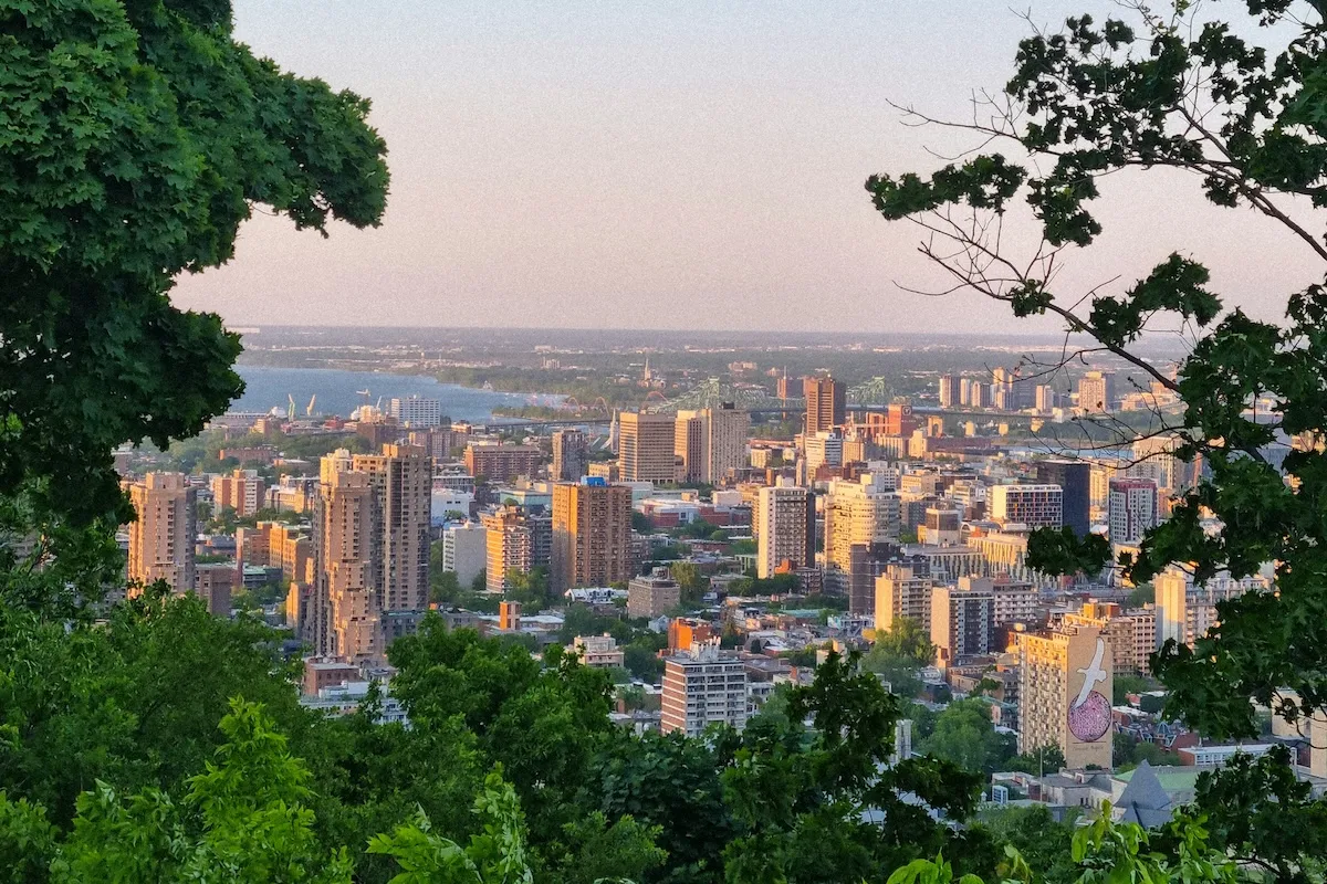 Montreal şehrinin modern binaları, geniş yeşil alanları ve nehir kıyısıyla çevrili, temiz bir havayı yansıtan aydınlık bir günde çekilmiş bu geniş açılı fotoğraf, kentin sürdürülebilir şehir olma vizyonunu vurguluyor.