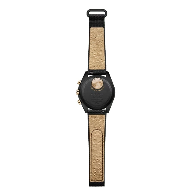 Omega ve Swatch iş birliğinin bir parçası olan, arkadan görünümde siyah Moonswatch kol saati; Ay'a Görev temalı arka kapağında dolunay görseli, Temmuz 20, 1969 tarihi ve kraterli bej renkli kayış detaylarıyla bu özel sınırlı üretim kol saatinin benzersiz tasarımını vurguluyor.