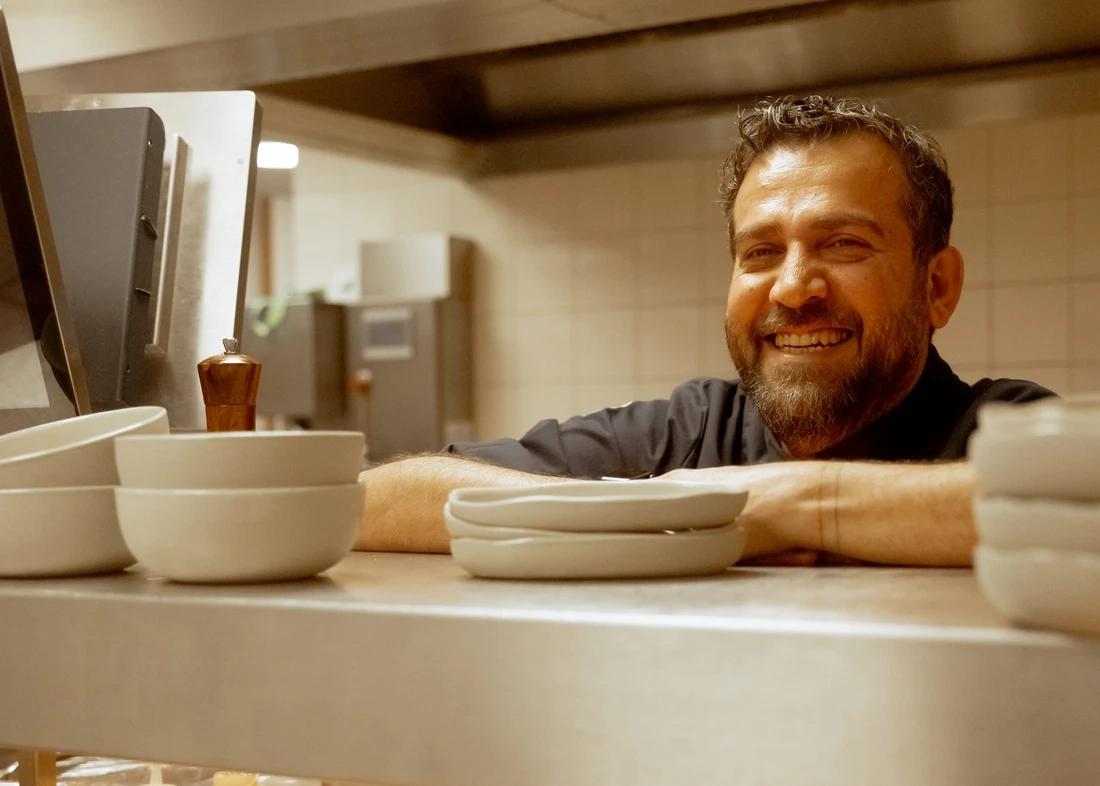 Şef Maksut Aşkar, Rotterdam'daki Fenix Müzesi'nin O Anatolian Café & Bakery adlı müze restoranının mutfağında, Anadolu lezzetlerini çağdaş yorumuyla sunarken sıcak bir gülümsemeyle poz veriyor; ön planda zarif açık renkli kaseler ve tabaklar, arkasında modern mutfak ekipmanları dikkat çekiyor, bu da müze restoranlarının gastronomi tutkunları için başlı başına bir seyahat nedeni olabileceğini vurguluyor.