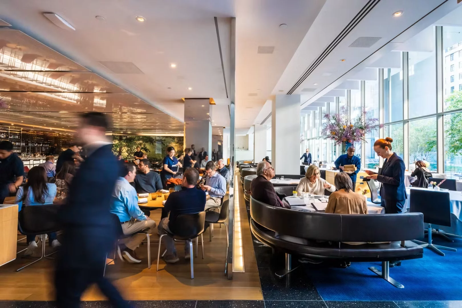 New York'taki ünlü The Modern müze restoranının aydınlık ve geniş salonunda, şık masalarda yemek yiyen misafirler ve özenli servis ekibi, büyük pencerelerden süzülen doğal ışık ve dışarıdaki yeşil bahçe manzarası eşliğinde çağdaş sanat ve gastronomiyi birleştiren eşsiz bir deneyimin tadını çıkarıyor.