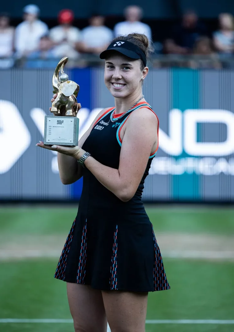 Berlin Tennis Open'da kazandığı fil figürlü kupayı gülümseyerek sergileyen Linda Noskova, kariyerindeki bu önemli zaferle yeşil kortta seyircilere doğru poz verirken, siyah tenis kıyafeti ve siperliğiyle dikkat çekiyor.