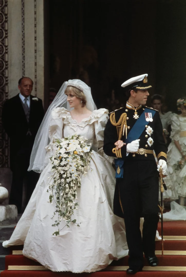 Prenses Diana, ipek tafta kumaşından yapılmış, hacimli kolları ve uzun kuyruğu olan ikonik gelinliğiyle, askeri üniformasıyla Prens Charles'ın yanında kırmızı halı kaplı merdivenlerden inerken Prenses Diana stili yolculuğunun romantik başlangıcını yansıtıyor.