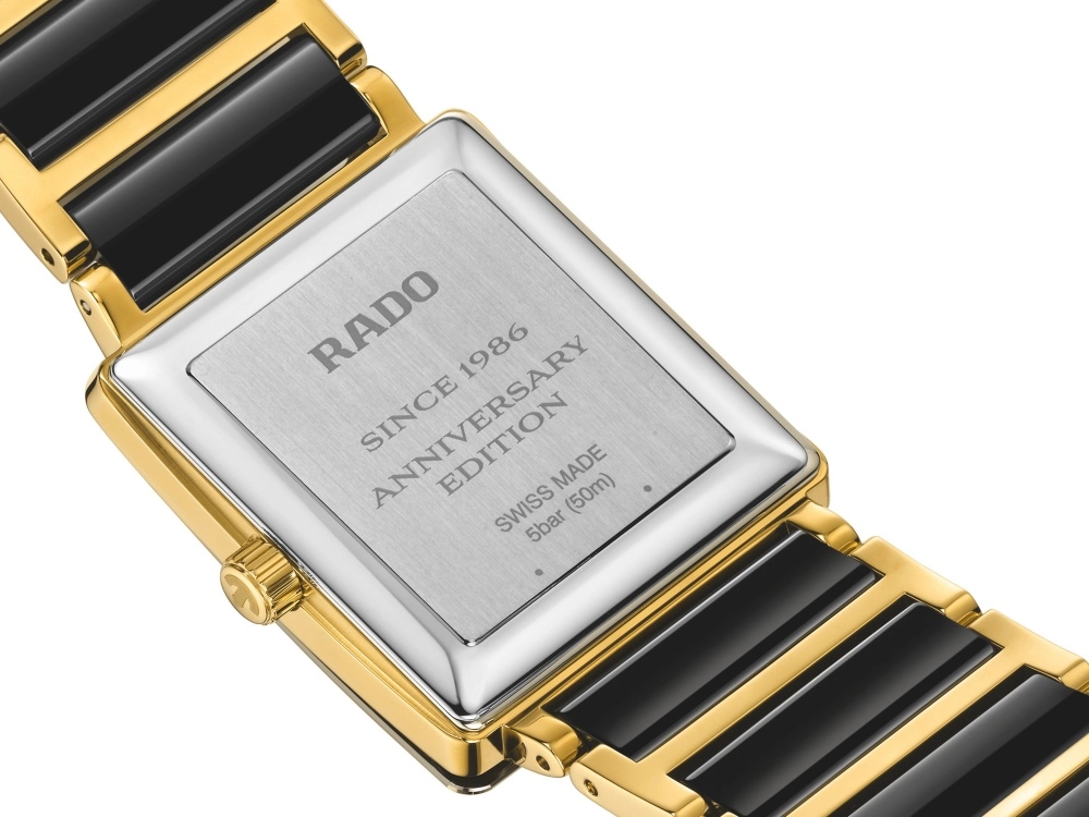 Rado Integral seramik saatin arka yüzünü gösteren bu detaylı görselde, saatin siyah seramik ve altın rengi bileziği, RADO, SINCE 1986, ANNIVERSARY EDITION ve SWISS MADE yazılı fırçalanmış metal kasası ile altın renkli kurma kolu belirgin bir şekilde yer alıyor.
