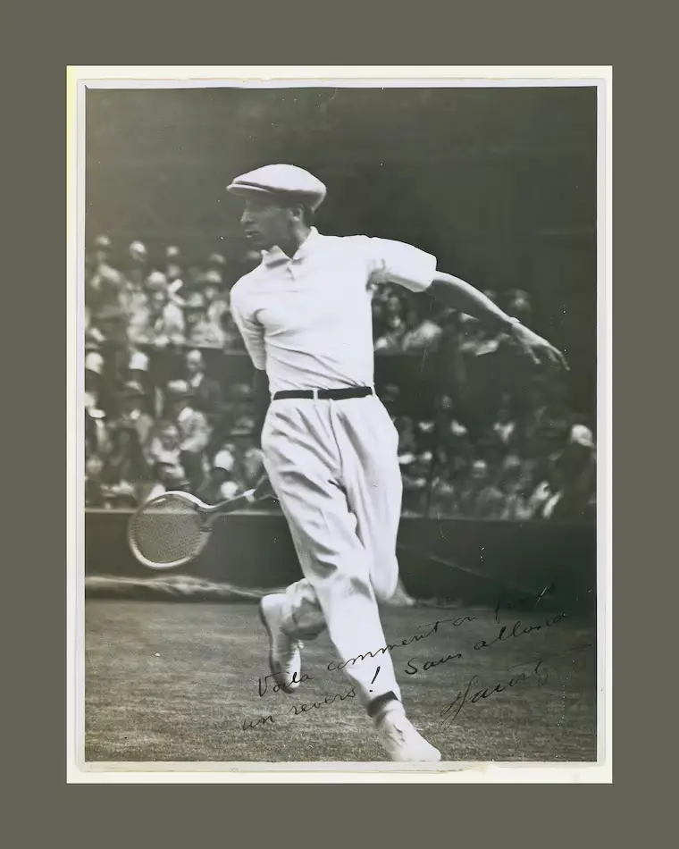 Underwood Lacoste arşivlerinden bu siyah beyaz fotoğrafta, efsanevi tenisçi Rene Lacoste, beyaz polo tişörtü, pantolonu ve kasketiyle bir tenis kortunda raketini ustaca savurarak dinamik bir vuruş anında kalabalık seyirci önünde resmedilmiş.